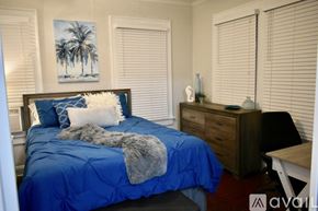 Tampa apartment for rent - A bedroom with a blue bedspread and a painting of palm trees on the wall.