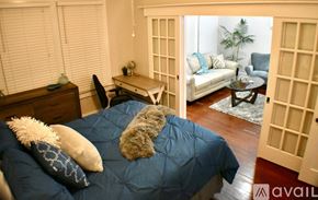 Tampa apartment for rent - A bedroom with a bed covered in a blue comforter and two pillows, a desk with a chair, and a couch in the background.