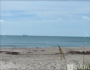 Cocoa Beach condo for rent - A beach with a ship in the distance and grass in the foreground.