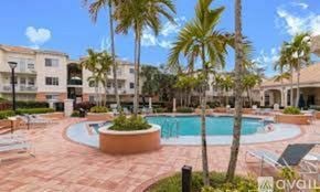 West Palm Beach condo for rent - A pool surrounded by palm trees and lounge chairs.