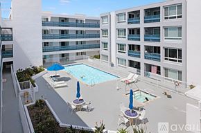 Oceanside apartment for rent - A pool area with chairs and umbrellas in front of apartment buildings.