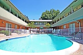 Dallas apartment for rent - A large swimming pool is surrounded by a metal fence and a building with red brick walls.