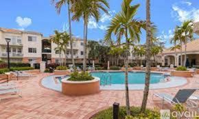 West Palm Beach condo for rent - A pool surrounded by palm trees and lounge chairs.