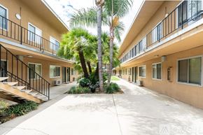 Azusa apartment for rent - A row of apartment buildings with balconies and a palm tree in the courtyard.
