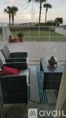 Vero Beach condo for rent - A patio with a table and chairs overlooking a fence and palm trees.