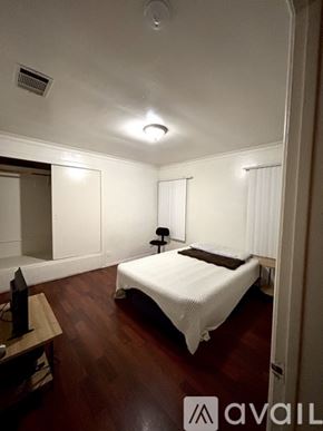 Los Angeles house for rent - A bedroom with a bed, lamp, and wooden floors.