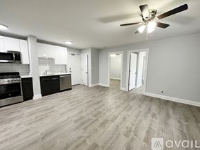 Chicago apartment for rent - A spacious living room with a ceiling fan and light fixture, hardwood flooring, and a kitchen area with stainless steel appliances.