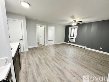 Chicago apartment for rent - A spacious room with a ceiling fan and light, and a kitchen area with white cabinets and a countertop.