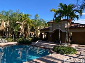 Royal Palm Beach townhouse for rent - A pool surrounded by palm trees and a building in the background.