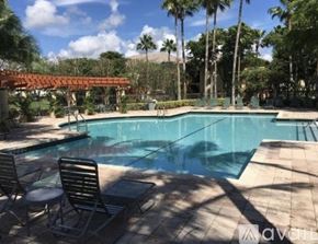 West Palm Beach condo for rent - A pool surrounded by palm trees and a shaded area.