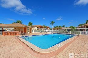 Naples condo for rent - A large outdoor swimming pool surrounded by a brick patio and a white fence.