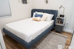 North Hollywood apartment for rent - A bed with a white sheet and a blue headboard is in a room with a lamp and a bookshelf.