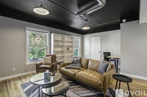 Grand Rapids apartment for rent - A living room with a brown leather couch, a glass coffee table, and a window with a view of trees.