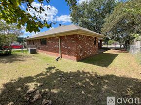 Overton apartment for rent - A house with a red brick exterior and a brown roof is situated in a grassy area with a dirt road in front.