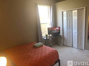 Apopka apartment for rent - A bedroom with a bed, a small table with a TV on it, and a window with curtains.