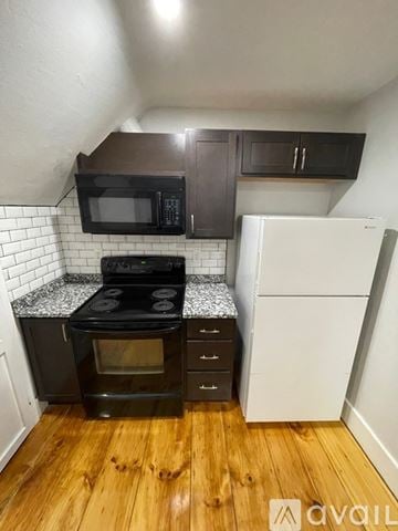 Lowell apartment for rent - A kitchen with a black oven and microwave, a white fridge, and wooden floors.