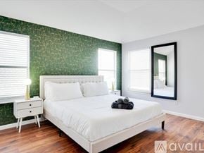 Haltom City house for rent - A bedroom with a white bed, a nightstand with a lamp, and a mirror on the wall.
