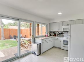 Irving house for rent - A kitchen with white cabinets and appliances, a dining table with chairs, and a sliding glass door leading to a backyard.