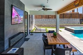 Lake Havasu City house for rent - A modern outdoor dining area with a wooden table and chairs, a television, and a pool.