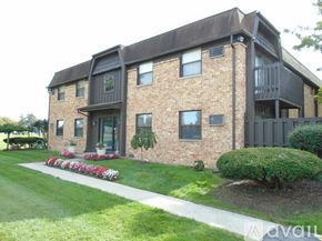 Maumee apartment for rent - A brick house with a balcony and a garden in front.