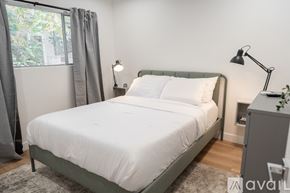 Los Angeles apartment for rent - A bed with a white comforter and two white pillows sits in a room with a grey headboard and a grey nightstand with a plant on top.