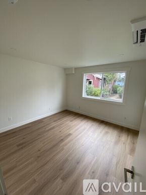Eureka house for rent - A room with wooden flooring and a window showing a view of a red building and trees.