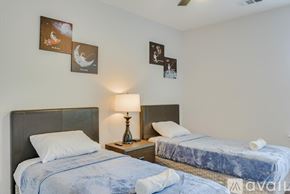 Dallas house for rent - A bedroom with two beds, one of which is made, and a lamp on a bedside table.