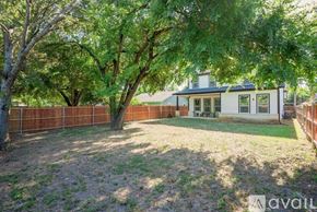 Dallas house for rent - A house with a white facade and a brown fence is surrounded by trees.