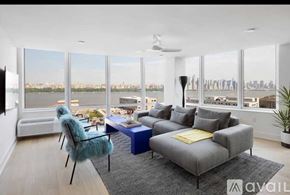 North Bergen condo for rent - A living room with a grey couch, a blue table, and a large window with a view of the city.