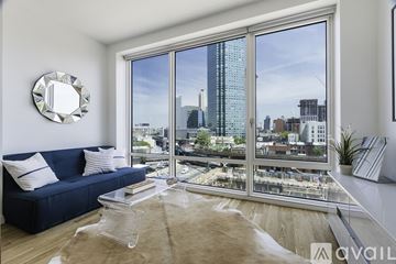 Queens apartment for rent - A living room with a blue couch and a large window overlooking a cityscape.