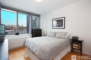 Manhattan apartment for rent - A bedroom with a large bed, a window with a view of the city, and a picture frame on the wall.