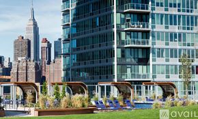 Manhattan apartment for rent - A modern building with a pool and lounge chairs in the foreground and the Empire State Building in the background.