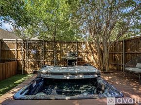 Dallas house for rent - A hot tub is in the middle of a backyard with a wooden fence and trees.