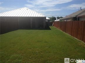 New Braunfels house for rent - A backyard with a wooden fence and a white building in the background.