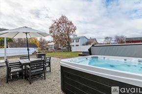 Rutland house for rent - A hot tub is in the foreground of a backyard with a table and chairs.