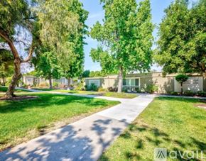 Laguna Woods townhouse for rent - A tree-lined pathway leads to a building in a sunny, green park.