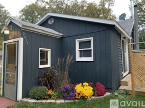 Bitely house for rent - A blue house with a white window and a door is surrounded by flowers.