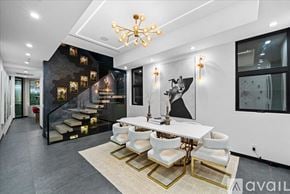 Los Angeles house for rent - A modern dining room with a white table and chairs, a chandelier, and a staircase with a black and gold design.