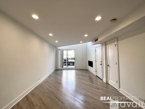 Chicago apartment for rent - A spacious room with wooden flooring and white walls, leading to a balcony.