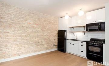 Chicago apartment for rent - A kitchen with a black refrigerator, white cabinets, and a brick wall.