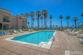 Oceanside apartment for rent - A swimming pool surrounded by palm trees and lounge chairs.