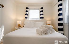 Miami house for rent - A bedroom with a white bed and striped curtains.