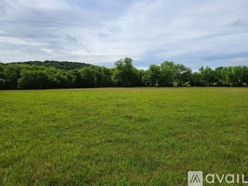Stilwell house for rent - A grassy field with trees in the distance under a blue sky with clouds.