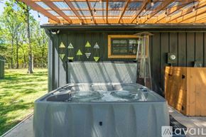 Greenville house for rent - A hot tub sits on a patio under a wooden roof with a fan and a window.
