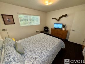 Manzanita house for rent - A bedroom with a bed, a lamp, a framed picture, a window with blinds, a wooden dresser with a laptop on top, and a decorative antler headboard.