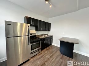 Chicago apartment for rent - A kitchen with a stainless steel refrigerator, black cabinets, and a wooden floor.