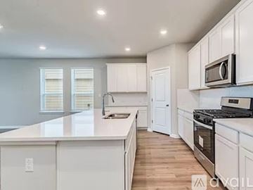 Dripping Springs house for rent - A kitchen with white cabinets and appliances, a large island, and a window with blinds.