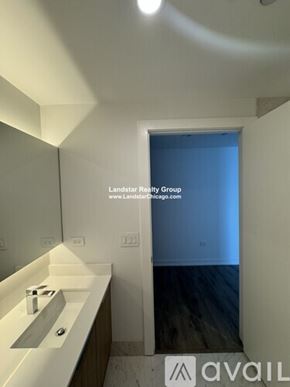 Chicago apartment for rent - A bathroom with a sink and mirror in the foreground and a doorway leading to a bedroom in the background.