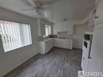 Bakersfield apartment for rent - A kitchen with white appliances and cabinets, a ceiling fan, and a window with blinds.
