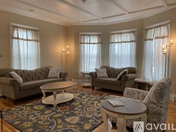 Watertown house for rent - A living room with a grey sofa, a grey armchair, a white coffee table, and a rug with a floral pattern.